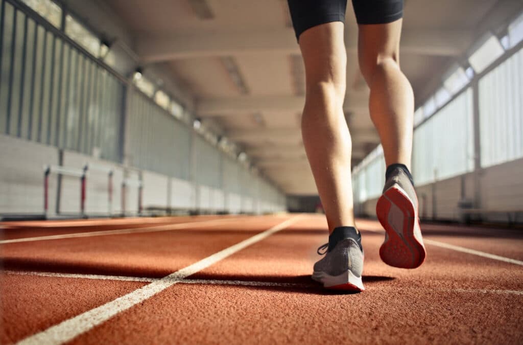 piernas de atleta corriendo en pista de atletismo en interior con zapatillas deportivas